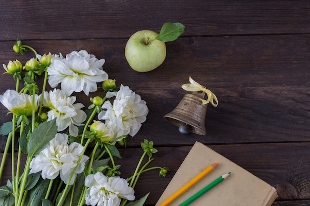 букет белых цветов, книга, карандаши (желтые и зеленые), старый колокольчик и зеленое яблоко