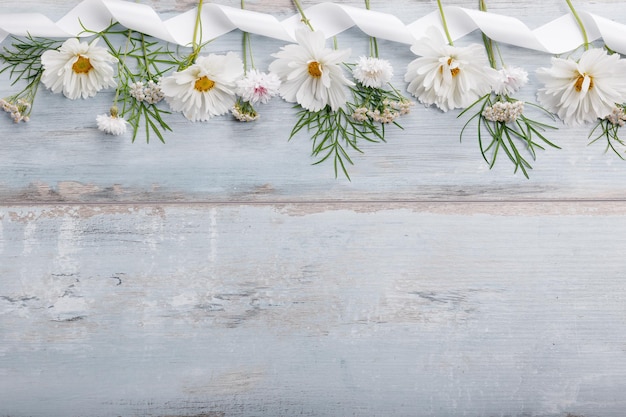 화이트 보드에 리본이 달린 흰색 꽃 코스메아 또는 코스모스의 꽃다발 수제 나무 테이블 배경 위에 정원 노란색 꽃 복사 공간이 있는 배경