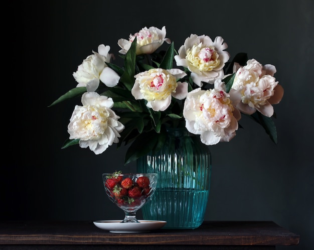 Bouquet of white peonies in a glass vase and strawberries. 