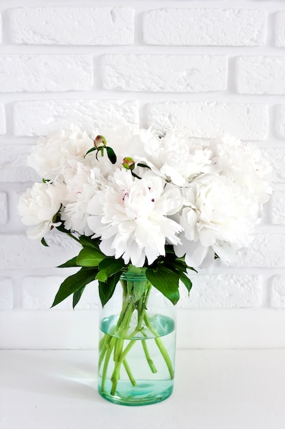 Photo bouquet of white peonies in a glass vase on a white break wall surface