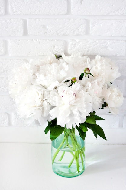 Bouquet of white peonies in a glass vase on a white break wall surface