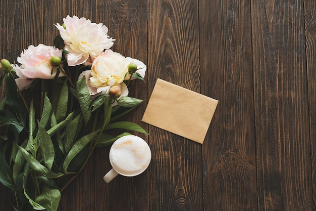 Bouquet white pink peonies flowers cup coffee and card on a\
wooden background flat lay minimalist aesthetic peonies beautiful\
card for mother\'s day or women\'s day