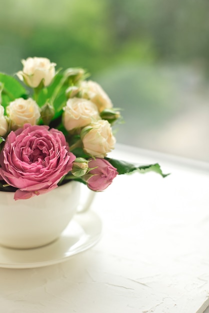 Foto bouquet di rose bianche in una tazza su un tavolo bianco di fronte alla finestra