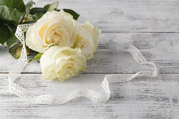 Bouquet of white roses decorated with ribbon on white wooden background