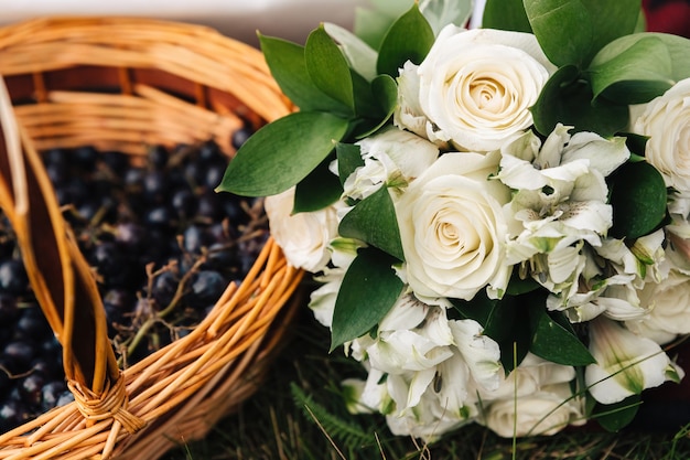 A bouquet of white roses lies next to a basket of grapes.
