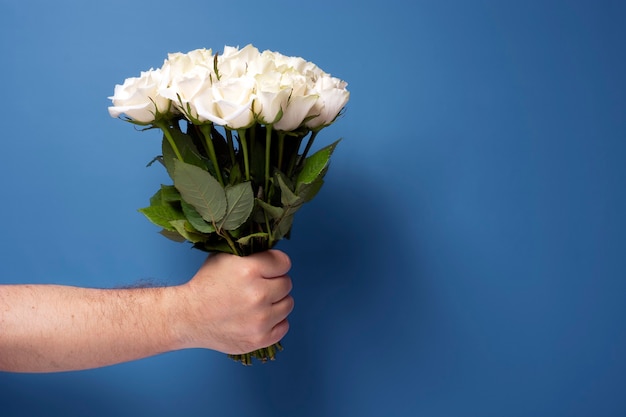 Bouquet di rose bianche in mano di un uomo su sfondo blu