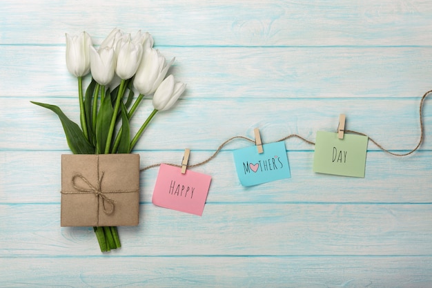 Foto un bouquet di tulipani bianchi e busta con adesivi a colori con mollette su una corda e tavole di legno blu. festa della mamma