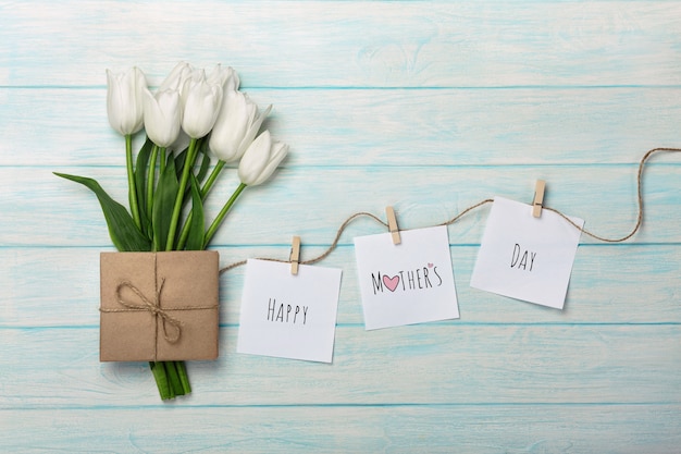 A bouquet of white tulips and envelope with a stickers with clothespins on a rope and blue wooden boards . Mother's day