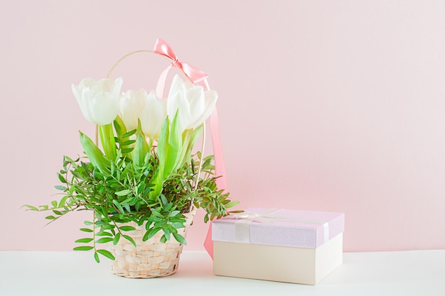 A bouquet of white tulips and a gift box on a pink background