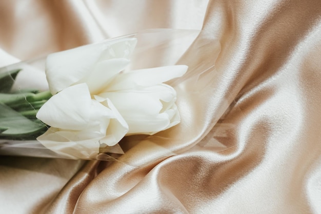 Bouquet of white tulips on silk golden nude satin background