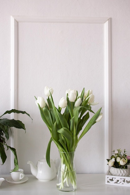 흰 튤립 꽃다발이 흰 탁자 위의 꽃병에 서 있다