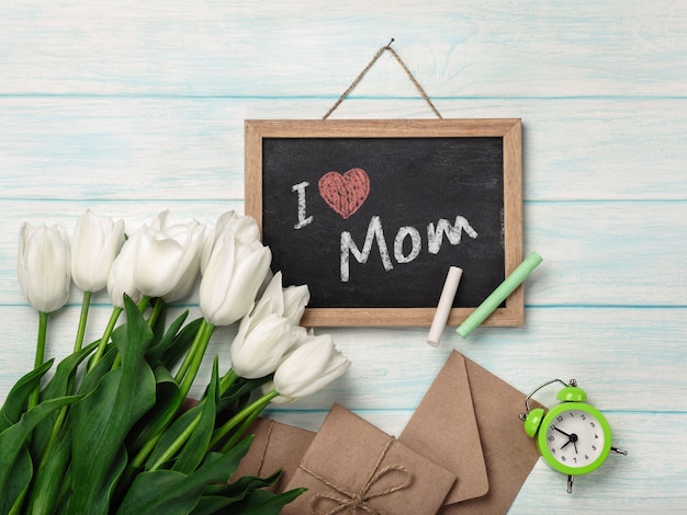 A bouquet of white tulips with chalk board and envelopes on blue wooden boards . Mother's day