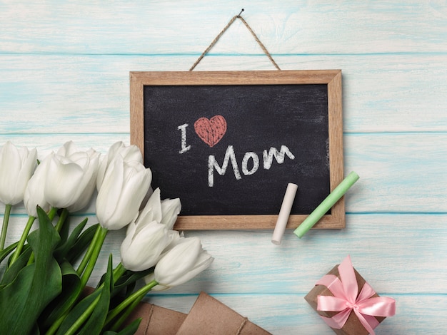 A bouquet of white tulips with chalk board, gift box envelopes on blue wooden boards . Mother's day