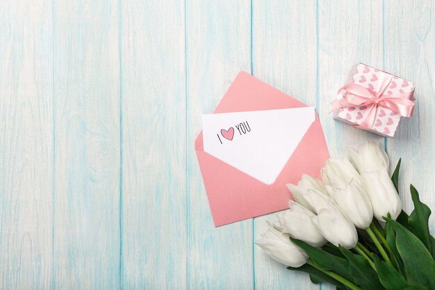 A bouquet of white tulips with a gift box, love note and color envelope on blue wooden boards