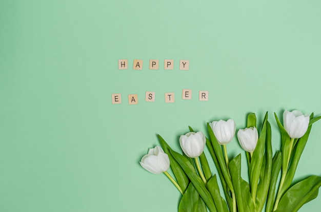 Bouquet of white tulips and the word Happy Easter on a green background, copy space, flat lay