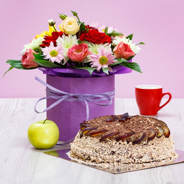 Букет полевых цветов, яблоко, шоколадный торт и чашка кофе на деревянных досках.