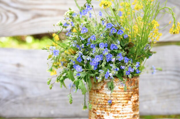 A bouquet of wildflowers in a rusty rustic jar against wooden planks.