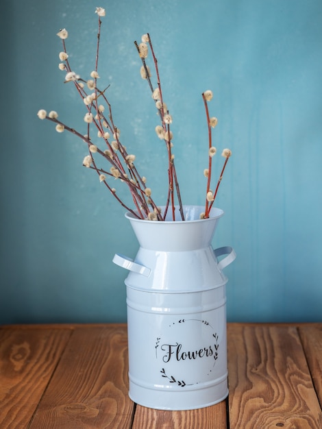 A bouquet of willow in a blue tall planter stands on a wooden table