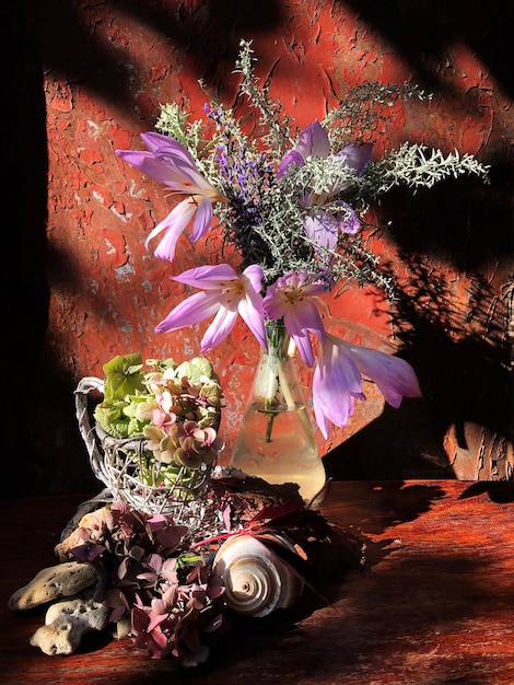 A bouquet with autumn flowers in a glass flask with pale pink flowers in a wooden decorative basket, sea shell and stones in the rays of the autumn sun.