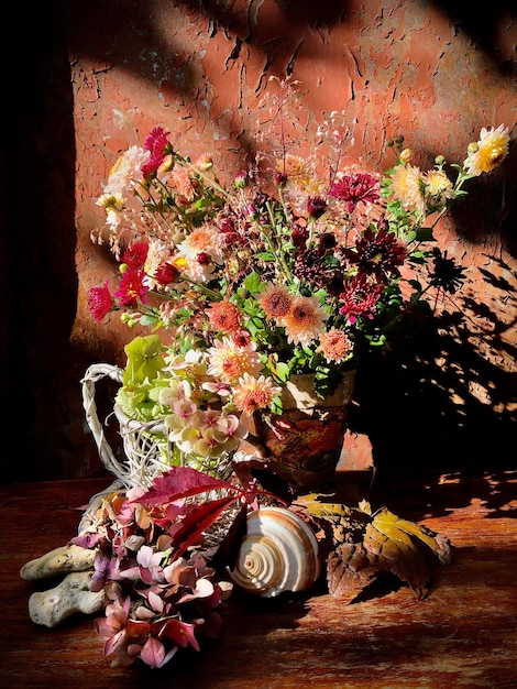 A bouquet with autumn flowers in a glass flask with pale pink flowers in a wooden decorative basket, sea shell and stones in the rays of the autumn sun.