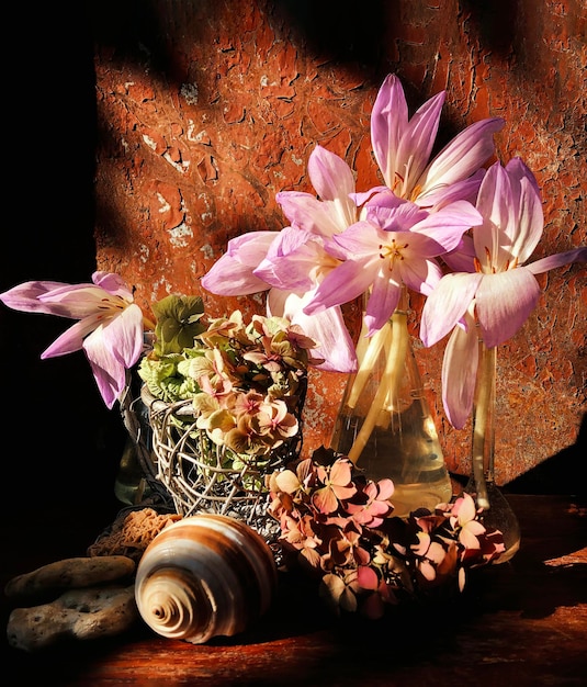 A bouquet with autumn flowers in a glass flask with pale pink flowers in a wooden decorative basket, sea shell and stones in the rays of the autumn sun.