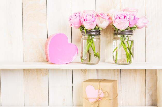 Bouquet with pink roses in mason jar on wood shelf.