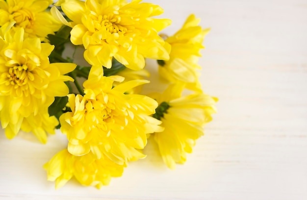 A bouquet of yellow chrysanthemums lies on a light wooden surface Selective focus