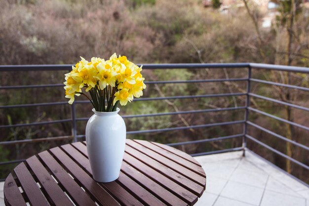 Bouquet of yellow daffodils in a white vase on a wooden table outdoor