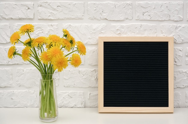 Bouquet yellow dandelion in vase and blank black letter board on table 