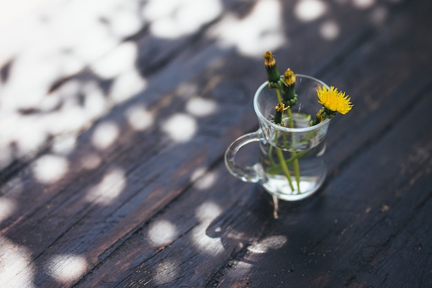 Bouquet of yellow dandelions in glass on grungy wood.