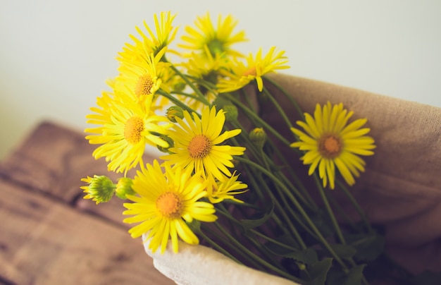 Bouquet of yellow flowers in a basket on wooden