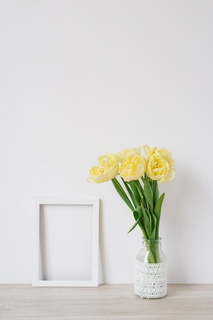 A bouquet of yellow flowers and an empty white frame for photos on a light background