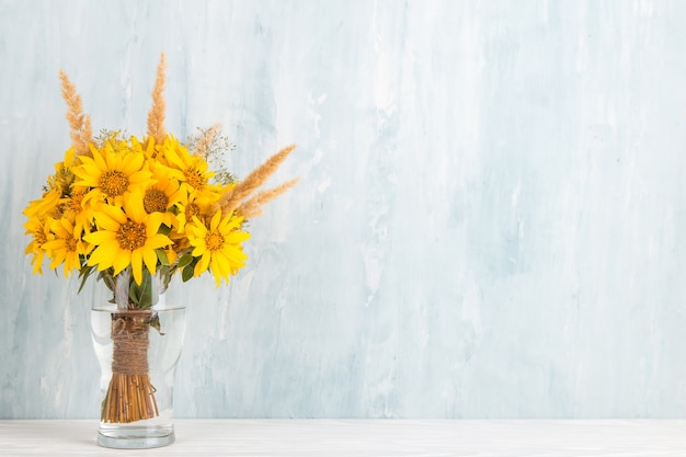 A bouquet of yellow flowers, sunflowers, in a glass vase on blue. Copy space.