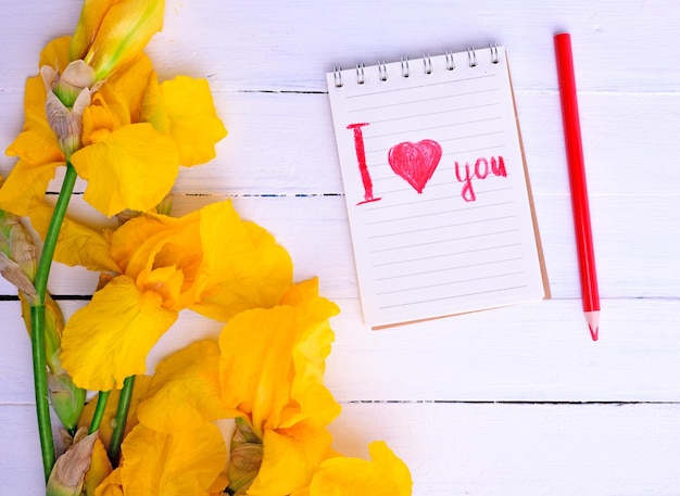 Photo bouquet of yellow irises and a notebook with an inscription red pencil on a white wooden background