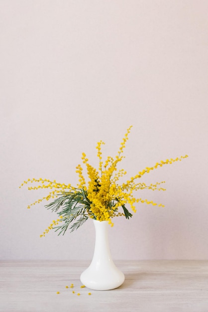 黄色のミモザの花の花束が白い陶器の花瓶に立っている 3 月 8 日のイースターのコンセプト