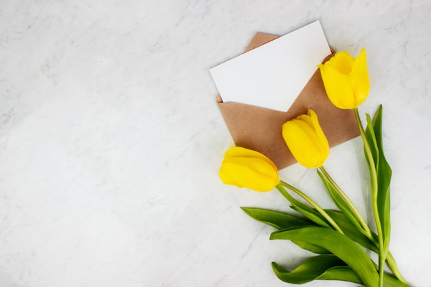 Bouquet of yellow tulips, envelope and letter flat lay on marble background