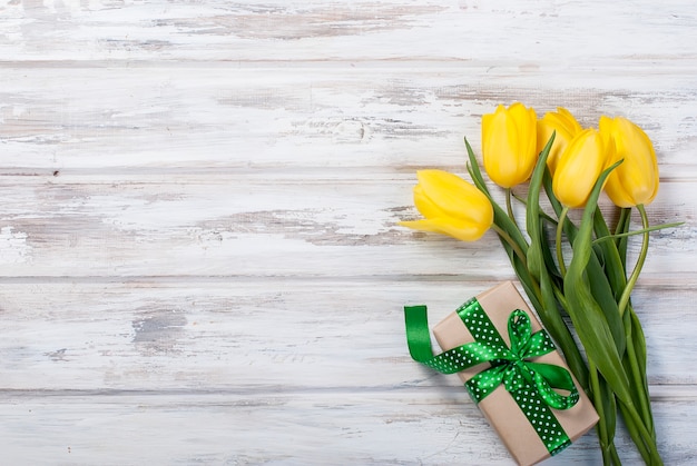 Bouquet of yellow tulips and a gift with a yellow ribbon on a wooden background