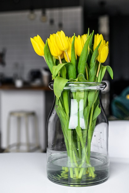 A bouquet of yellow Tulips in a glass vase on the background of the apartment interior. Side view