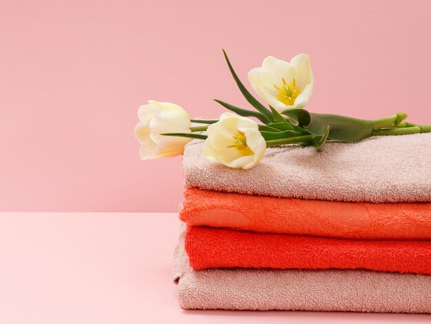 Bouquet of yellow tulips and stacked towels on a pink background