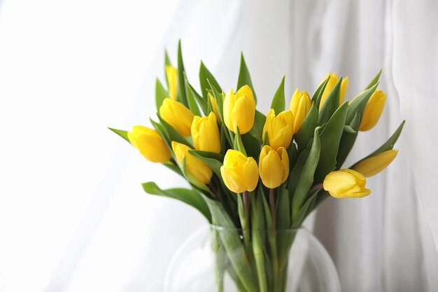 A bouquet of yellow tulips in a vase on the windowsill. A gift to a woman's day from yellow tulip flowers. Beautiful yellow flowers in a vase by the window.