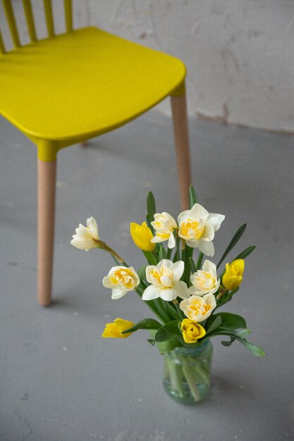 A bouquet of yellow and white tulips next to a yellow chair on a light background