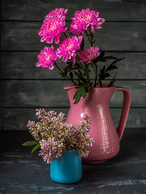 木製の背景にピンクのクリスアンテムとライラックの花束が陶器の花瓶に埋め込まれています