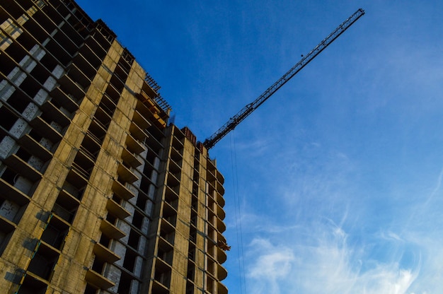 Bouw van een nieuw gebouw met meerdere verdiepingen, een hoge oranje kraan, bouwt vloeren die zwaar en grijs dragen