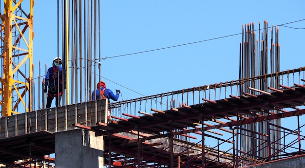 Bouwconstructieplaats en werknemer permanent op staal en beton materiaal en blauwe hemel.