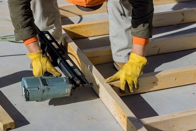 Bouwer binnen houten huisman in het spijkeren van houten balken werkt voor de bouw met behulp van een luchthamer van