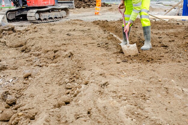 Bouwer die schop gebruikt om stoepranden en voetpaden schoon te maken die zuur bedekt zijn met teelaarde