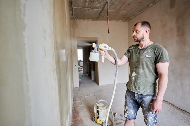 Bouwer is aan het schilderen met airbrush muur huis reparatie groot volume werk is zichtbaar op de achtergrond