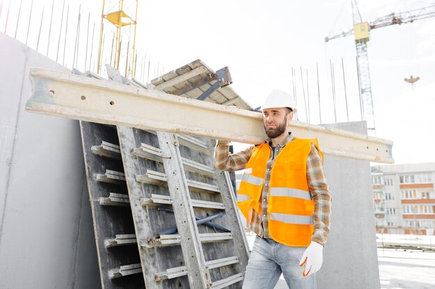 Bouwer man in bouwvakker en vest met hout op de bouwplaats in zijn werkdag