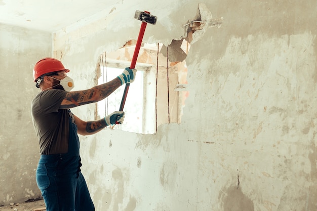 Foto bouwer met een hamer in zijn handen breekt de betonnen muur