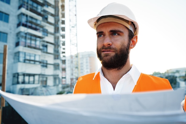 Bouwer of architect met veiligheidshelm die toezicht houdt op een project en naar blauwdrukken kijkt